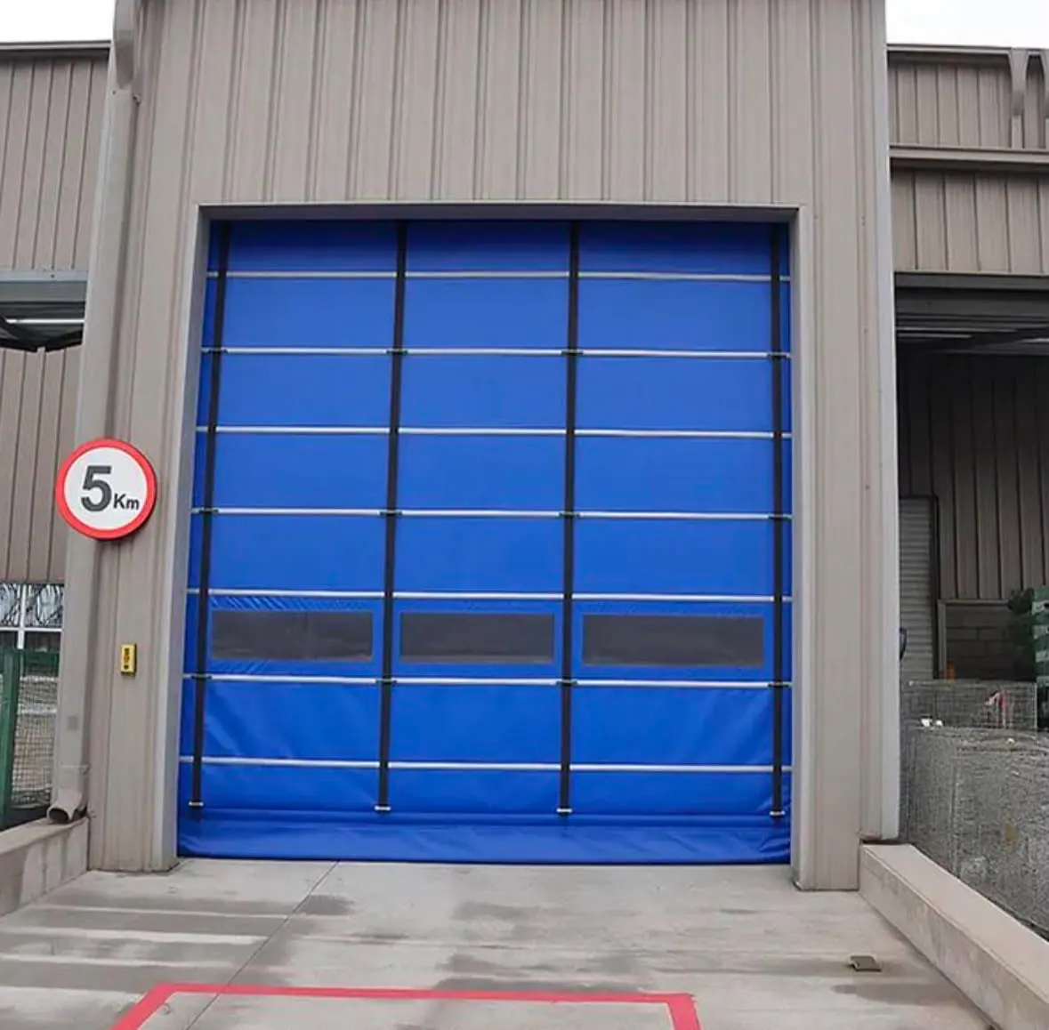 Fabrika dış cephesinde rüzgar barlı mavi katlanır PVC branda kapı